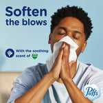 Person blowing their nose into a tissue with headline 'Soften the blows' and Puffs and Vicks logos on a light blue background.