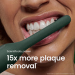 Close-up lifestyle shot of a person using a dark green quip electric toothbrush near their teeth