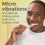 Person brushing teeth with a yellow Philips toothbrush head beside text about micro vibrations and tapered bristles