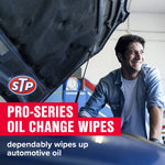 Smiling person leaning by a car with the hood up and STP logo and red banner text promoting Pro‑Series oil change wipes