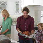 Kitchen lifestyle scene of an adult carrying a foil roaster pan with a cooked roast while a child looks on