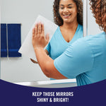 Person wiping a mirror with a Sparkle paper towel, smiling while cleaning a bathroom mirror