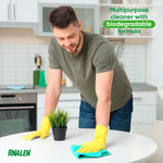 Man wearing yellow cleaning gloves wiping a round white table in a kitchen, with Pinalen logo and text noting a biodegradable multipurpose cleaner.