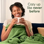 Person wrapped in a green blanket smiling and holding a mug with text reading Cozy up like never before