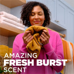 Lifestyle image of a person smelling a towel with overlay text 'Amazing Fresh Burst scent' and bright laundry setting