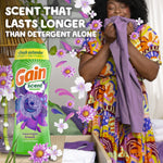Person smelling a purple garment beside a Gain scent booster bottle with floating flowers and text about lasting scent