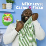 Smiling person smelling a green-and-white striped shirt with a Gain product image and 'Next Level Clean & Fresh' headline on blue background.