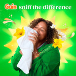 Person happily smelling a white towel with Gain branding and decorative flowers and slogan 'sniff the difference' behind them