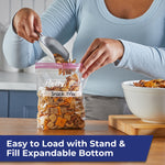 Person scooping snack mix into a Hefty quart stand-and-fill bag labeled Snack Mix on a kitchen counter