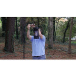 Person installing a lit Black Flag bug zapper on a tall metal pole in a wooded backyard setting