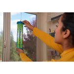 Person in yellow shirt reaching up to hang a RESCUE! TrapStik near a window with shelving and outdoor view behind