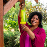 Person hanging a translucent neon-yellow RESCUE! yellowjacket trap outdoors beneath a wooden porch beam.
