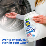 Person holding an all free clear Mighty Pacs tub near an open washing machine drum with a pac visible in the other hand