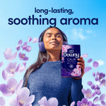 Person wearing headphones holding a Downy CALM box as purple flower petals float around with 'soothing aroma' headline.
