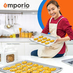 Smiling person in apron holding an Emporio aluminum baking sheet with cookies, additional sheet and cooling rack on countertop