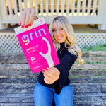 Person holding a magenta Grin Smooth floss picks pouch toward the camera while seated on an outdoor bench