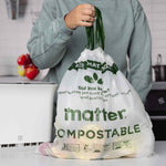 Person holding a full Matter compostable drawstring bag by green handles in a kitchen setting