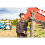 Person holding a reusable POP! Fly Trap hung on a fence post in a rural setting with barn and tractor in background
