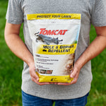 Lifestyle image of person holding a Tomcat Mole & Gopher Repellent bag standing on a lawn