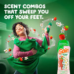 Person hugging a green sweater with floating strawberries and flowers and a Gain Tango bottle at right