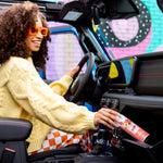 Smiling person inside a car reaching toward the dashboard while holding a Citrus Magic Georgia Peach spray can