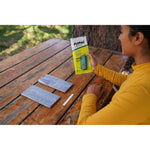 Person seated at picnic table holding FlyPad package with two foil-wrapped traps and instruction strip laid out