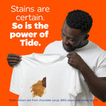 Smiling person inspecting a white T-shirt with a visible brown stain and copy reading So is the power of Tide
