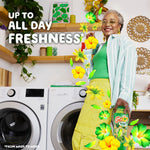 Smiling person in a laundry room holding a Gain scent booster with floral graphics and text 'up to all day freshness'