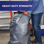 Person lifting a full gray Hefty Steelsak trash bag from a can demonstrating heavy duty strength with banner text above