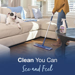 Lifestyle scene of a person mopping hardwood floor with a Bona mop while a dog lounges on a sofa nearby