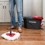 Close view of a person mopping a hardwood floor with an O-Cedar mop and EasyWring bucket visible in background