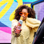 Person holding a Citrus Magic Georgia Peach car spray can toward the camera in front of colorful graffiti