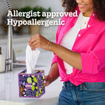 Smiling person at a counter pulling a patterned Kleenex cube tissue from a decorative box, hypoallergenic claim