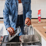 Person recycling a plastic bottle at a kitchen counter with a Febreze Watermelon spray can on the counter in background