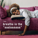 Lifestyle image of a smiling person reclining on a magenta couch with overlaid text 'breathe in the "mmhmmm"'.