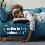 Person smiling and reclining on a teal sofa above copy reading breathe in the “mmhmmm”