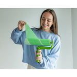 Smiling person pulling a green adhesive sheet from an Evercare lint roller while holding the handle