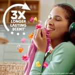 Person smiling while smelling a pink garment with 3X longer lasting scent graphic and floral accents