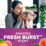 Person smelling a soft sweater with closed eyes above a purple panel reading Amazing Fresh Burst scent and fruit and flower visuals.