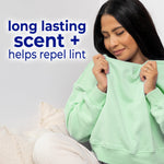 Person smelling a green sweatshirt with copy ‘long lasting scent + helps repel lint’ in a lifestyle image promoting Snuggle freshness