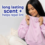 Person holding a pink sweatshirt to their face beside text reading “long lasting scent + helps repel lint” on light background