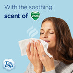 Person holding a tissue to their face with eyes closed and 'With the soothing scent of Vicks' text and Puffs logo on blue background.