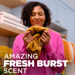 Lifestyle image of a smiling person smelling a yellow towel with overlaid text promoting the product’s Fresh Burst scent
