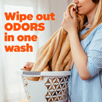 Person smelling a soft towel over a laundry basket with bold text promoting wiping out odors in one wash.