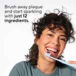 Smiling person holding a toothbrush near their mouth with overlay text promoting brushing with just 12 ingredients, lifestyle-style product image.