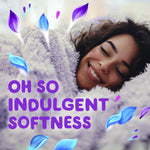 Close-up of a person smiling while snuggled in a plush blanket with 'Oh so indulgent softness' text and Gain petal graphics