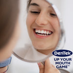 Person smiling into a hand mirror with DenTek logo and 'Up Your Mouth Game' slogan at lower right
