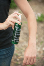 Person spraying a green Bug Soother bottle onto their forearm outdoors, bottle and hand in clear view.