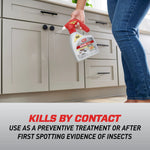 Person spraying Ortho Home Defense Max along baseboard in a kitchen while holding the bottle by the red trigger