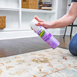 Person using an OdoBan lavender disinfectant aerosol to spray a rug in a living room setting